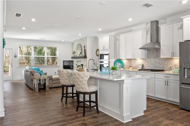 kitchen with open floor plan, visible vents, appliances with stainless steel finishes, and wall chimney range hood