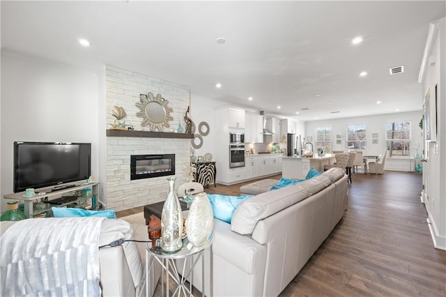 living room featuring recessed lighting, visible vents, a stone fireplace, and dark wood finished floors