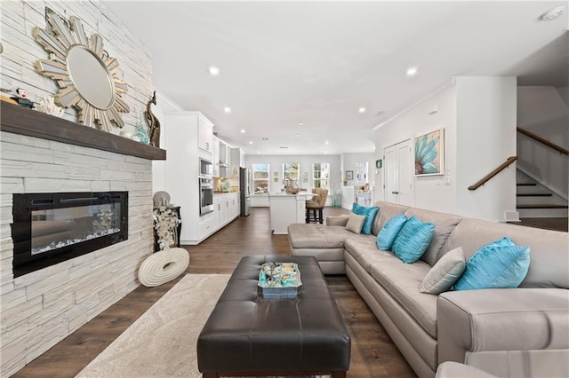 living area with recessed lighting, dark wood-style flooring, ornamental molding, stairs, and a stone fireplace