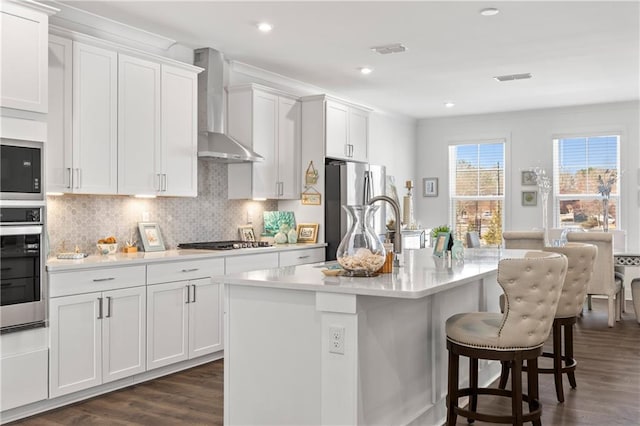 kitchen with wall chimney range hood, dark wood finished floors, light countertops, appliances with stainless steel finishes, and a kitchen breakfast bar