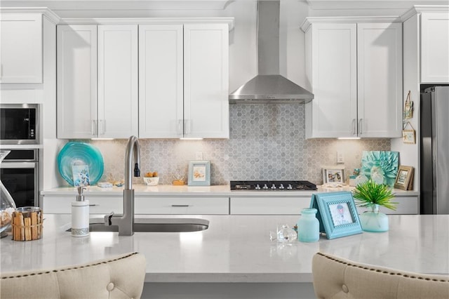 kitchen featuring white cabinetry, wall chimney exhaust hood, backsplash, and stainless steel appliances