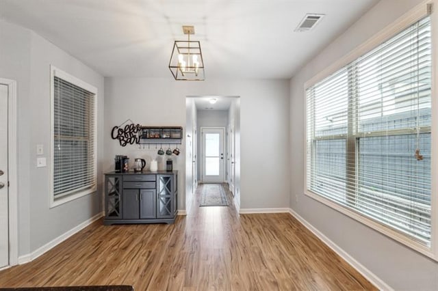 unfurnished dining area featuring visible vents, baseboards, wood finished floors, and a notable chandelier