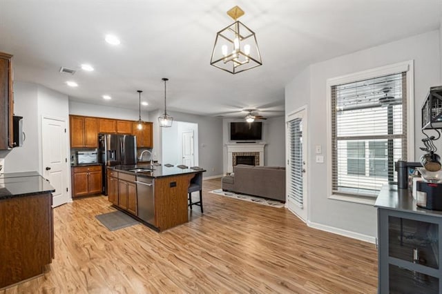 kitchen featuring dark countertops, stainless steel dishwasher, a sink, light wood-type flooring, and a fireplace