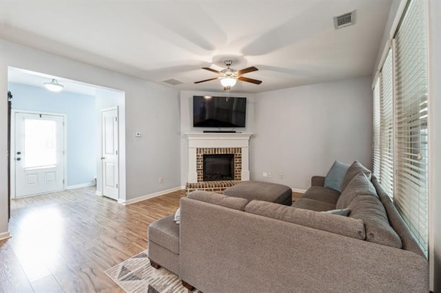living room featuring light wood-type flooring, baseboards, visible vents, ceiling fan, and a fireplace