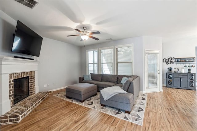 living room with baseboards, visible vents, a ceiling fan, wood finished floors, and a fireplace