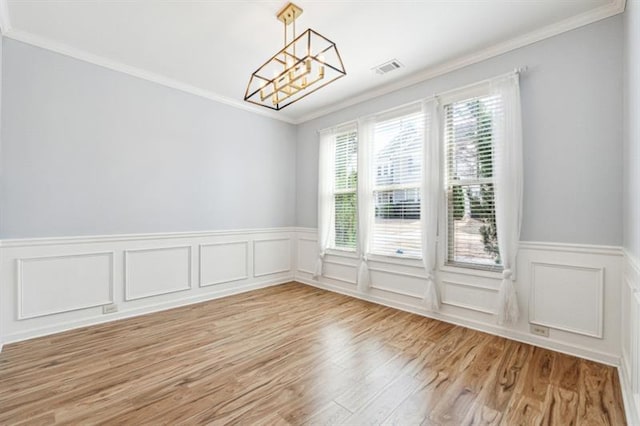 unfurnished dining area with light wood finished floors, crown molding, wainscoting, a chandelier, and a decorative wall