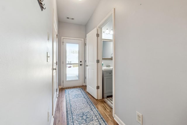 doorway to outside with light wood-style floors, visible vents, baseboards, and a sink