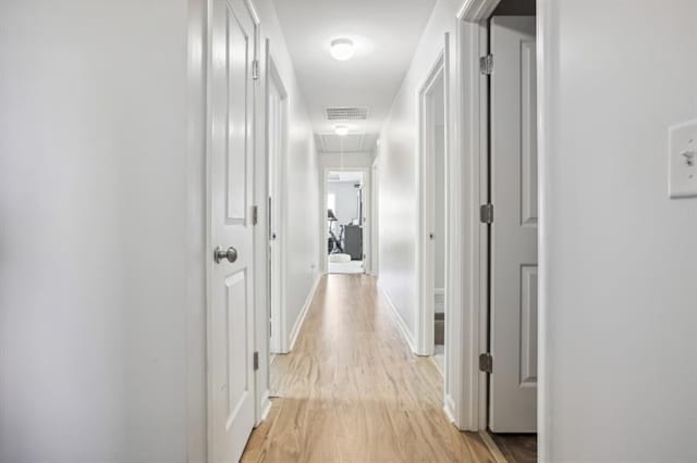 hallway featuring attic access, light wood-style floors, visible vents, and baseboards