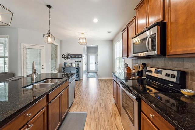 kitchen featuring light wood finished floors, brown cabinetry, a sink, and appliances with stainless steel finishes