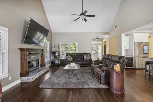 living room featuring dark hardwood / wood-style flooring, high vaulted ceiling, ceiling fan, and a stone fireplace