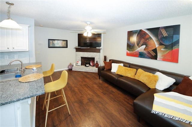 living room featuring sink, ceiling fan, a brick fireplace, dark wood-type flooring, and a textured ceiling