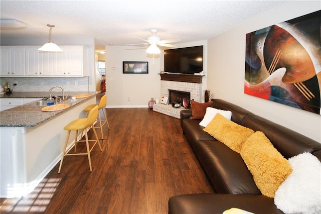 living room featuring ceiling fan, dark hardwood / wood-style floors, sink, and a brick fireplace