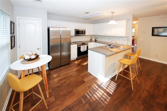 kitchen featuring decorative light fixtures, white cabinets, a kitchen breakfast bar, kitchen peninsula, and stainless steel appliances