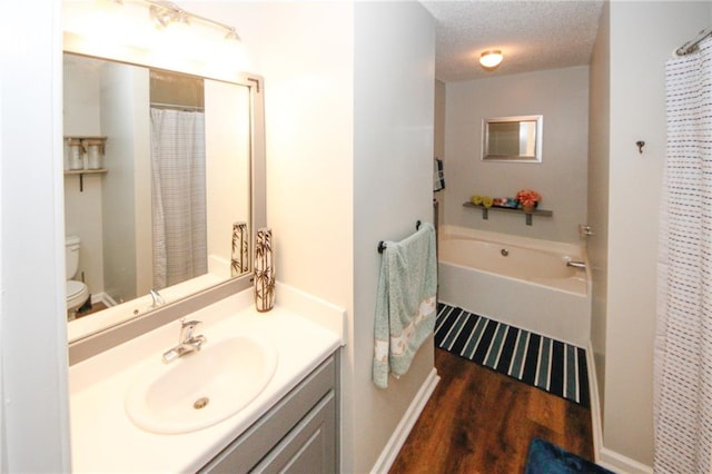 bathroom featuring vanity, wood-type flooring, a textured ceiling, a tub, and toilet