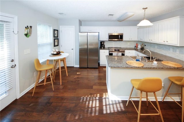 kitchen featuring white cabinetry, light stone counters, hanging light fixtures, kitchen peninsula, and stainless steel appliances