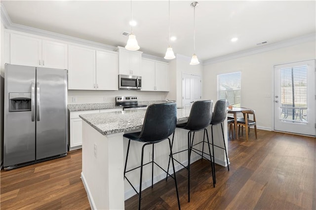 kitchen with appliances with stainless steel finishes, decorative light fixtures, white cabinetry, a kitchen island with sink, and light stone counters