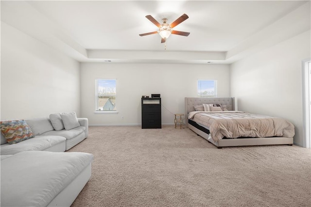 bedroom with ceiling fan, a tray ceiling, and light colored carpet