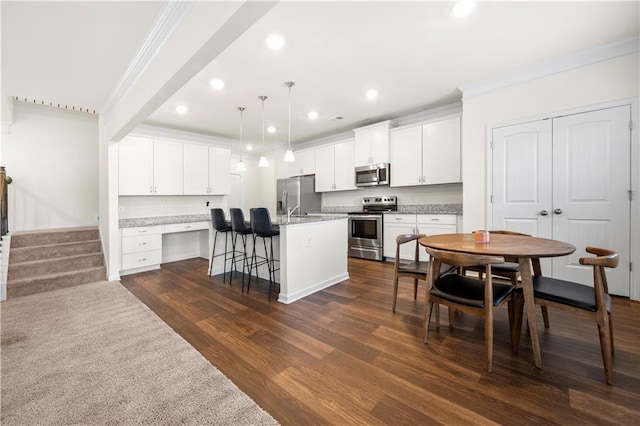 kitchen featuring appliances with stainless steel finishes, dark hardwood / wood-style floors, a breakfast bar area, white cabinets, and a center island with sink