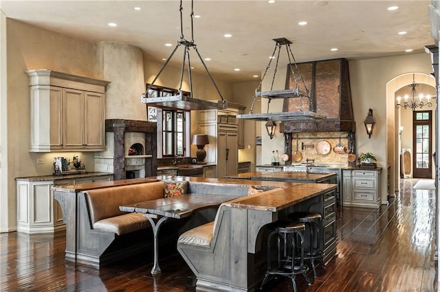 kitchen featuring arched walkways, a fireplace, a large island, dark wood-style floors, and dark stone countertops