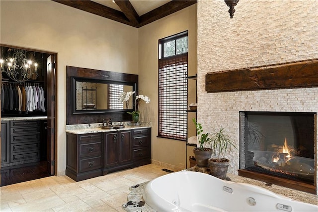 bathroom with a tub to relax in, baseboards, a walk in closet, vanity, and a fireplace