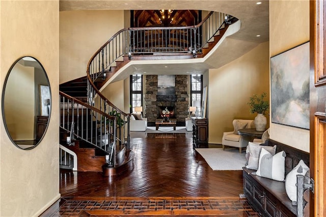 foyer with stairway, a stone fireplace, a towering ceiling, and wood finished floors