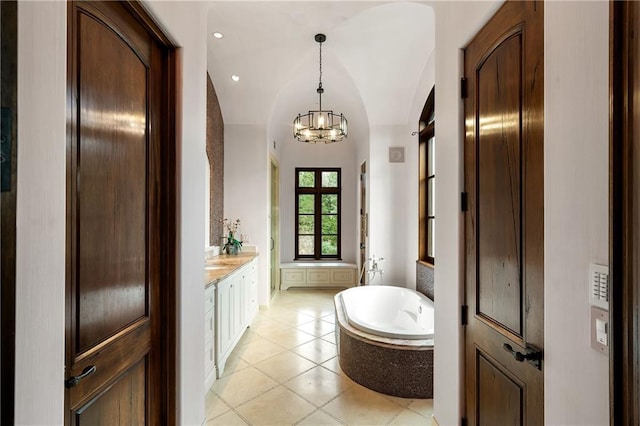 full bathroom featuring an inviting chandelier, tile patterned flooring, vaulted ceiling, vanity, and a bath