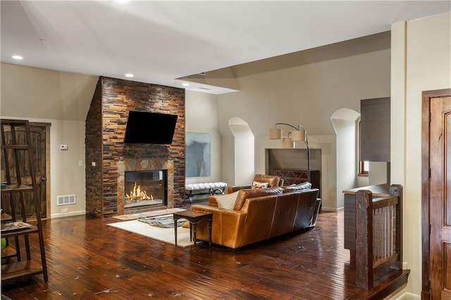 living room featuring arched walkways, visible vents, dark wood finished floors, and a fireplace