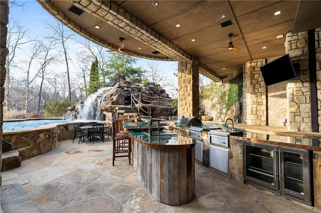 view of patio featuring outdoor dining area, outdoor wet bar, area for grilling, a sink, and a ceiling fan