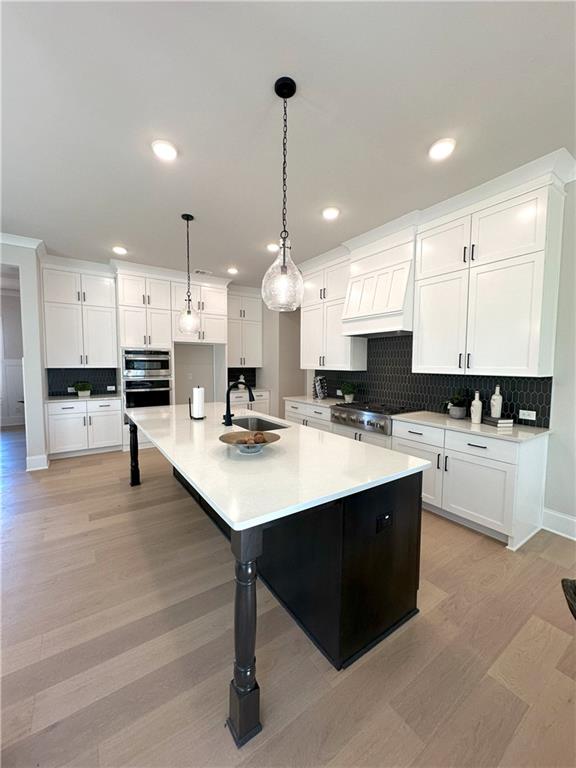 kitchen with pendant lighting, sink, white cabinetry, and an island with sink