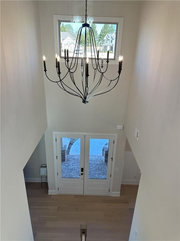 foyer entrance with french doors, hardwood / wood-style floors, and an inviting chandelier