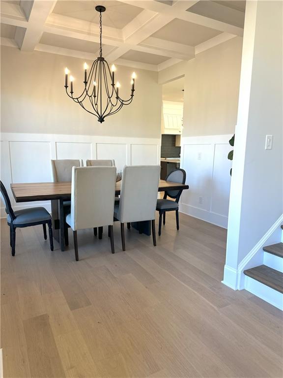 dining space with coffered ceiling, beam ceiling, and light hardwood / wood-style flooring