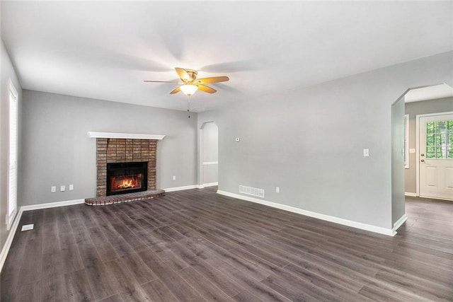 2722 Spring Side Ct, Douglasville, GA 30135 - unfurnished living room featuring arched walkways, a ceiling fan, a brick fireplace, dark wood-style flooring, and baseboards