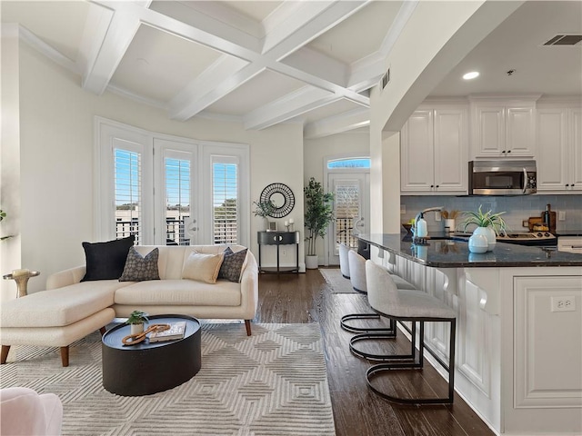 living room with dark wood-type flooring, coffered ceiling, sink, ornamental molding, and beamed ceiling