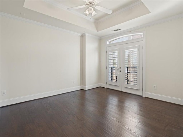 empty room featuring dark hardwood / wood-style flooring, ornamental molding, ceiling fan, a raised ceiling, and french doors