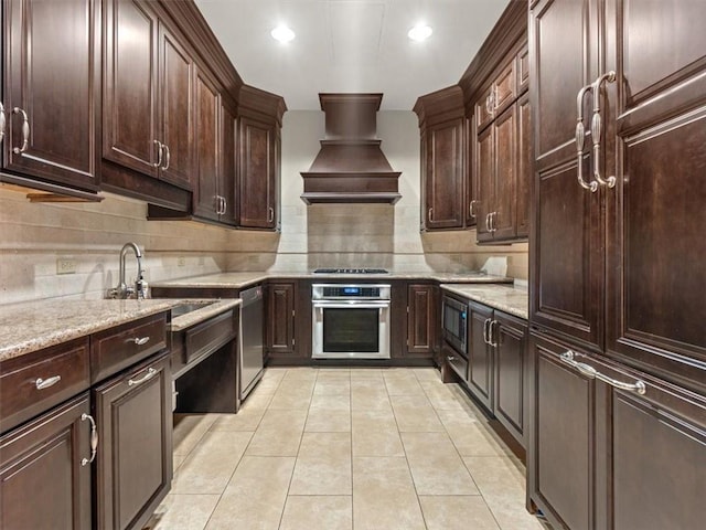 kitchen with custom exhaust hood, appliances with stainless steel finishes, light tile patterned floors, and light stone counters