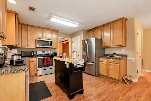 3265 Watson Gate Rd, Loganville, GA 30052 - kitchen featuring appliances with stainless steel finishes, light wood finished floors, a kitchen island, baseboards, and dark countertops