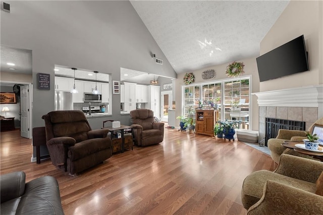 69 Maple Leaf Ct, Hoschton, GA 30548 - living area with high vaulted ceiling, a tile fireplace, wood finished floors, and a textured ceiling