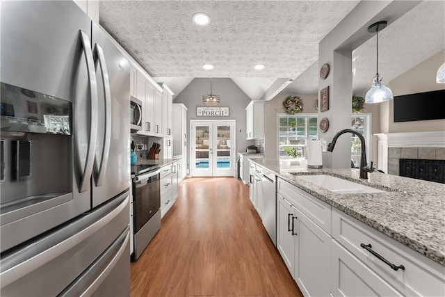 69 Maple Leaf Ct, Hoschton, GA 30548 - kitchen with stainless steel appliances, vaulted ceiling, white cabinetry, decorative light fixtures, and light wood-type flooring