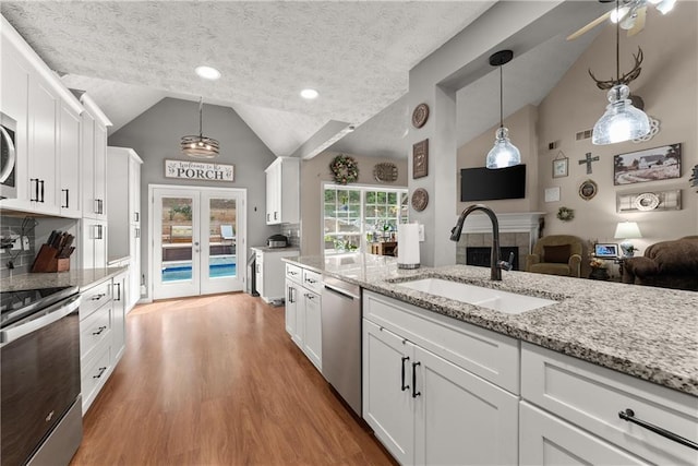 69 Maple Leaf Ct, Hoschton, GA 30548 - kitchen featuring appliances with stainless steel finishes, lofted ceiling, white cabinets, wood finished floors, and a tiled fireplace