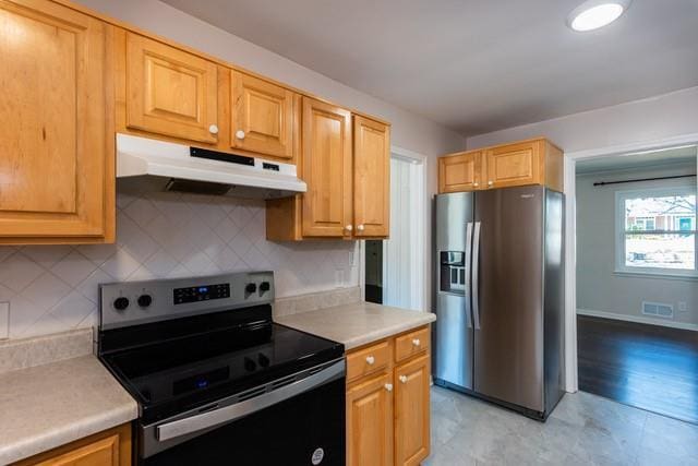 kitchen featuring visible vents, under cabinet range hood, range with electric stovetop, stainless steel fridge with ice dispenser, and light countertops