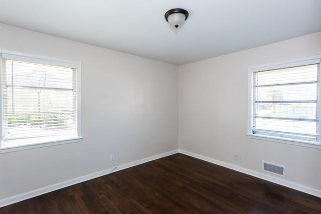 empty room featuring visible vents, baseboards, and dark wood-type flooring