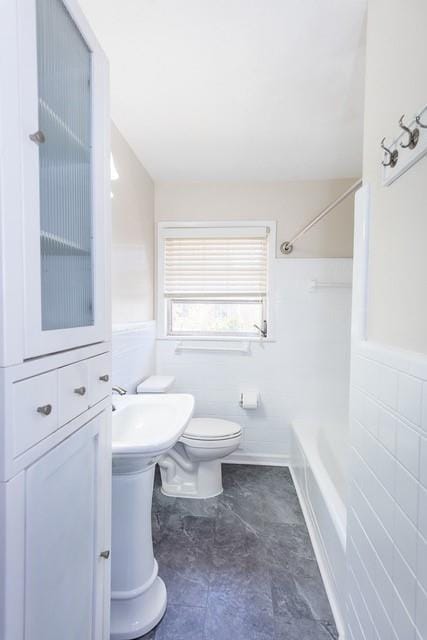 full bathroom featuring wainscoting, toilet, tile walls, and  shower combination