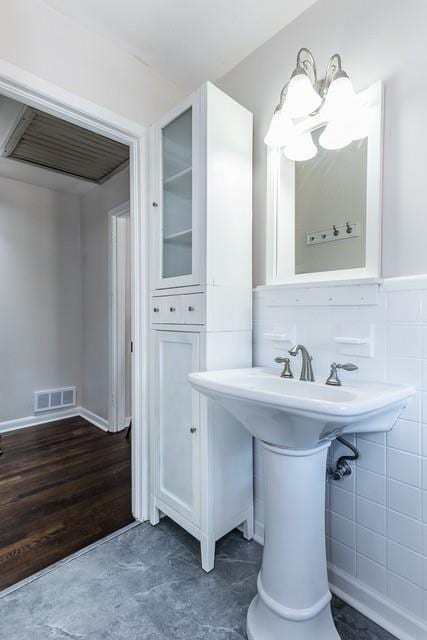 bathroom featuring a sink, tile walls, visible vents, and wainscoting