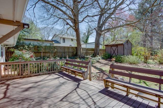 wooden terrace with an outdoor structure, a storage unit, and fence