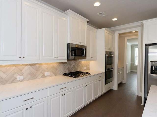 kitchen featuring stainless steel appliances, visible vents, white cabinetry, light countertops, and decorative backsplash