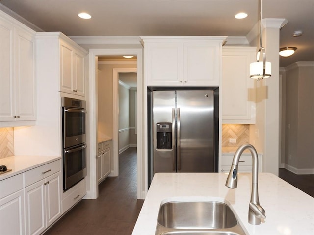 kitchen featuring decorative light fixtures, crown molding, stainless steel appliances, white cabinetry, and a sink