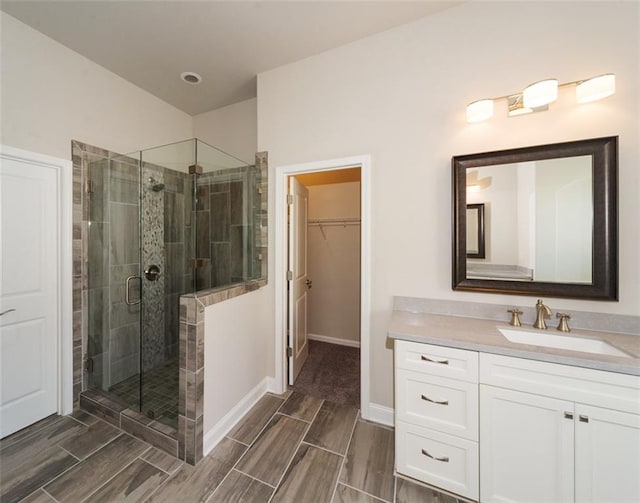 bathroom featuring baseboards, wood tiled floor, a walk in closet, vanity, and a shower stall