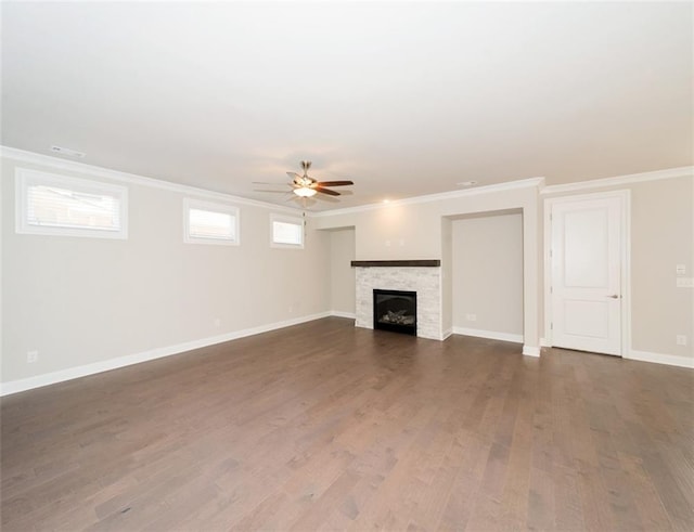 unfurnished living room with baseboards, a ceiling fan, dark wood-type flooring, crown molding, and a stone fireplace