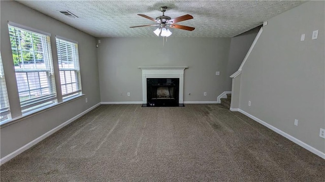 unfurnished living room featuring ceiling fan, a textured ceiling, plenty of natural light, a fireplace, and stairs