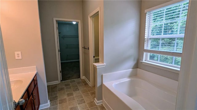 full bath with a bath, vanity, a walk in closet, and baseboards